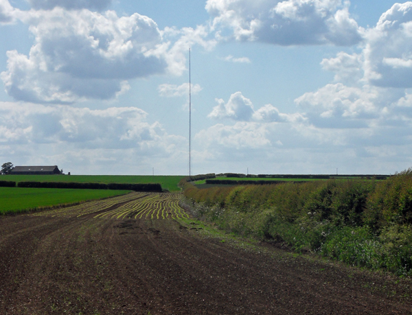 Meteorological mast standing in open terrain beneath an atmospheric sky